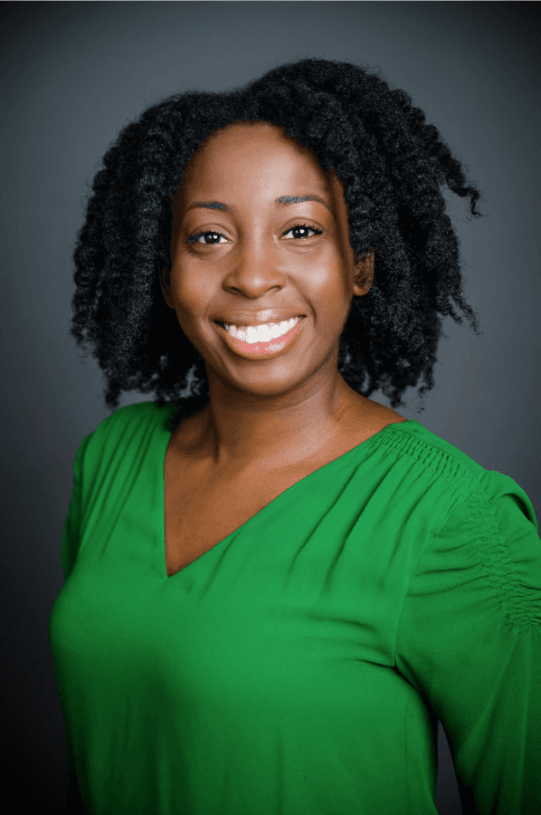 Woamn with dark hair in a green blouse headshot against gray