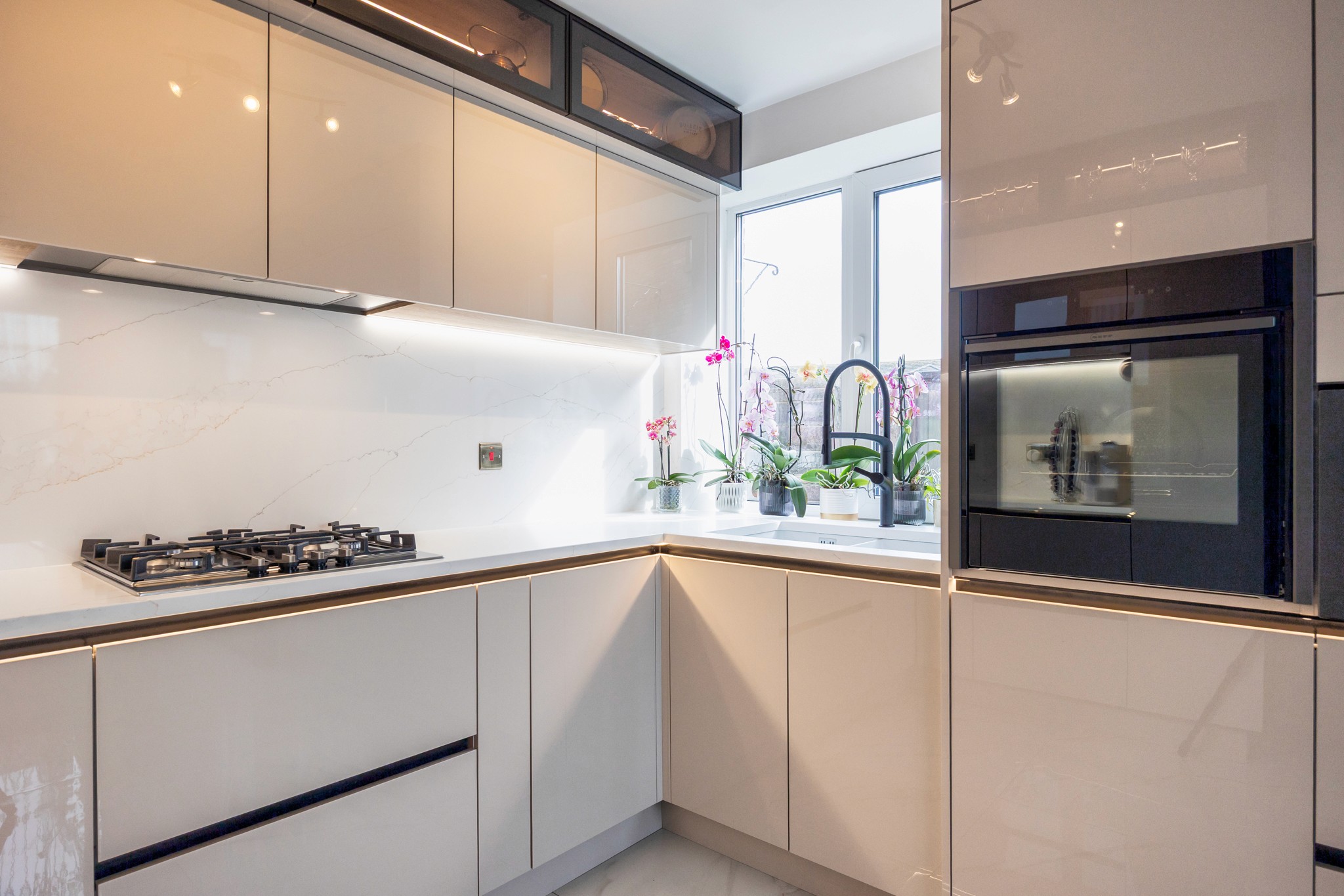 Modern two-story home with large glass windows, warmly lit interiors, and a balcony. Surrounded by trees and a manicured lawn at dusk. Cozy ambiance.