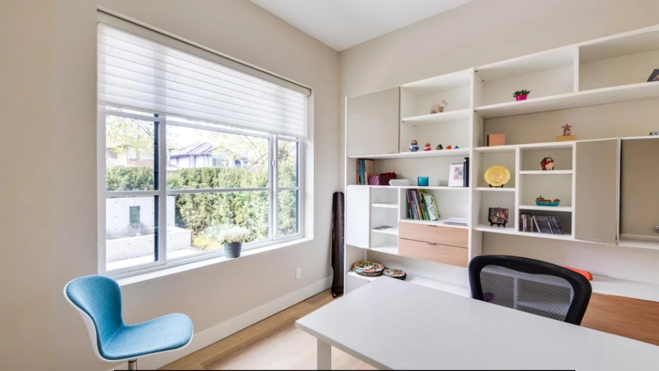 Custom home office with floor-to-ceiling built-in shelving, integrated desk space, modern chair, and large window overlooking landscaped yard