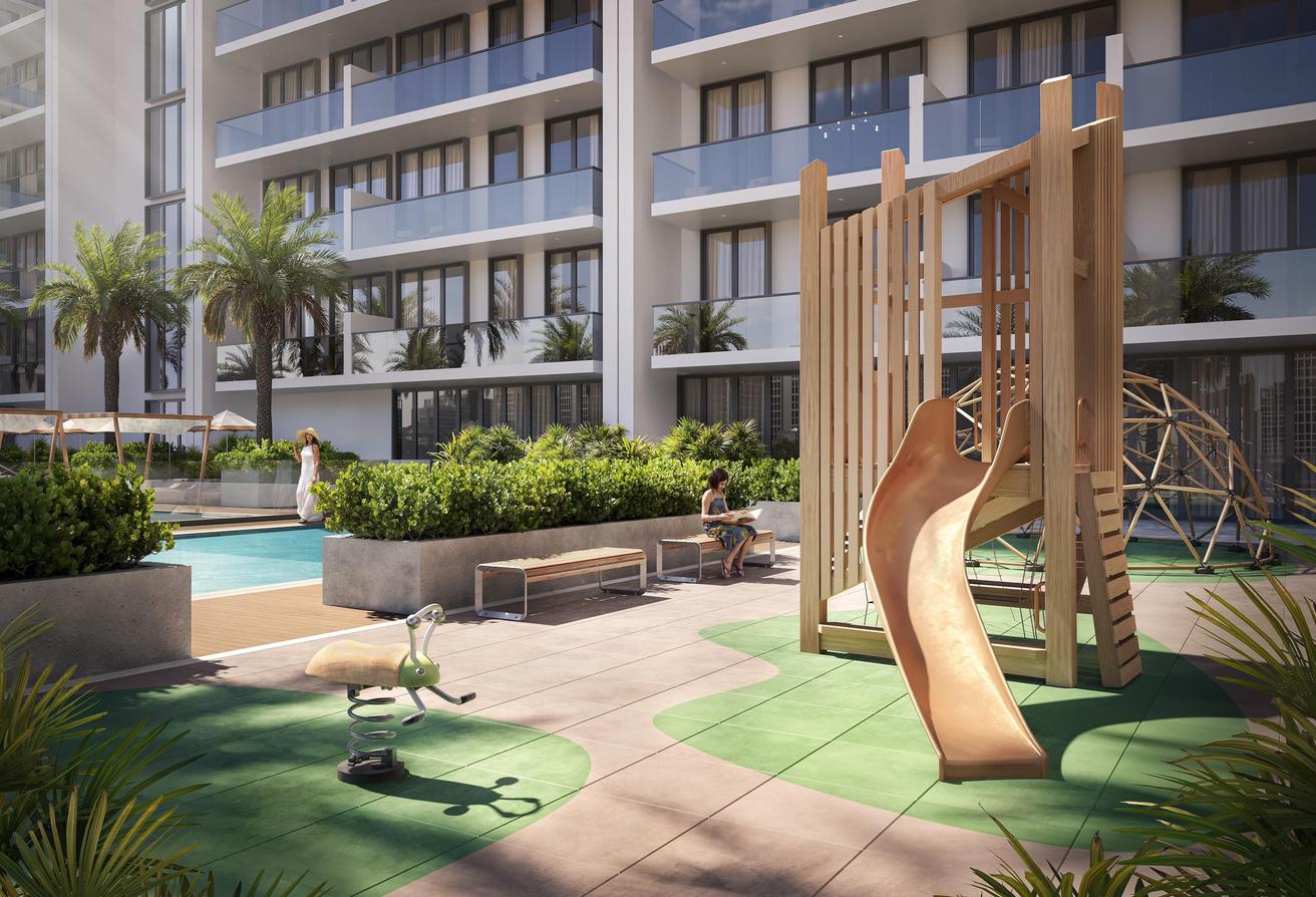 Children's play area and landscaped garden near poolside at Binghatti Amberhall residential project in Dubai
