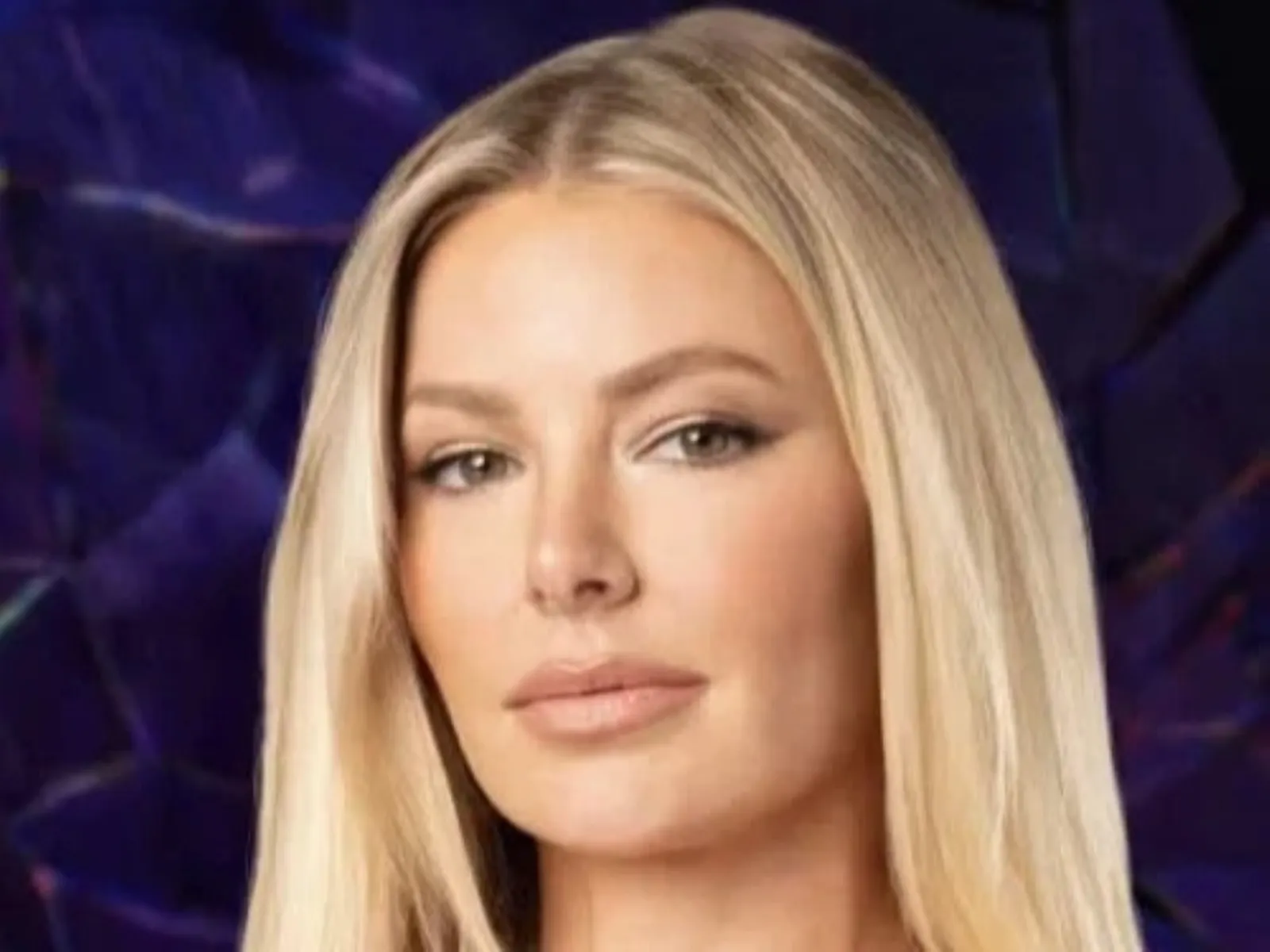 A woman with long blonde hair is posed against a dark, abstract background with deep blue and purple hues.
