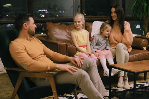 A photo of a mother sitting on couch with two daughters and father on chair next to couch