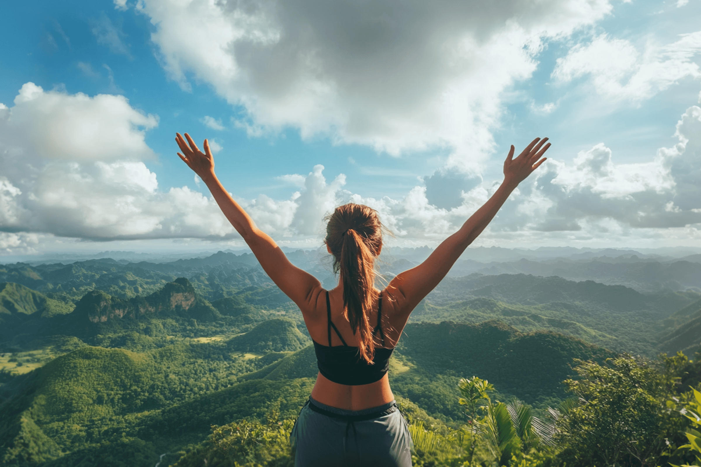 Woman standing on a hilltop with arms raised over green valleys