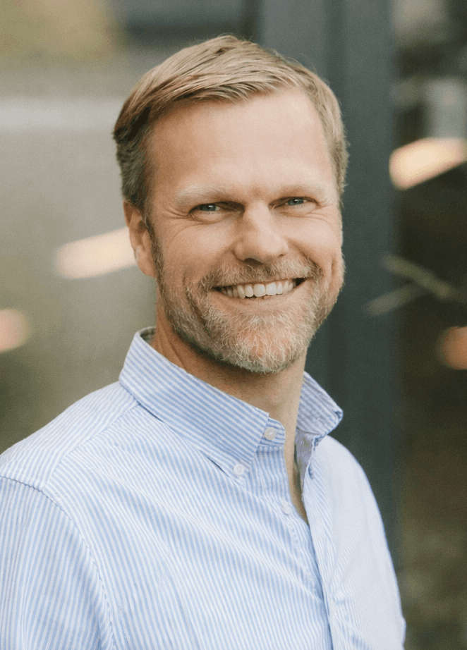 A young woman with long dark hair smiles confidently while crossing her arms in a modern indoor setting.