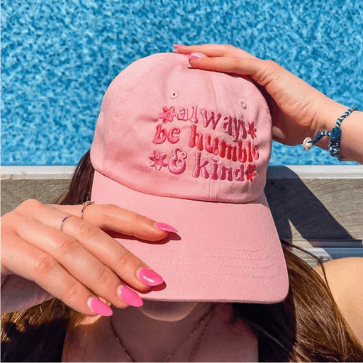 Pink hat with "always be humble & kind" embroidered, woman by pool with pink nails.