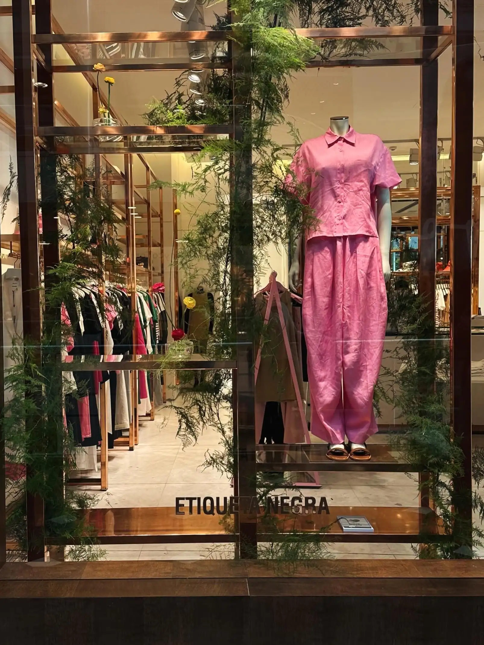 Vidriera de tienda Etiqueta Negra con maniquí en conjunto rosa y decoración botánica para exhibición primaveral.