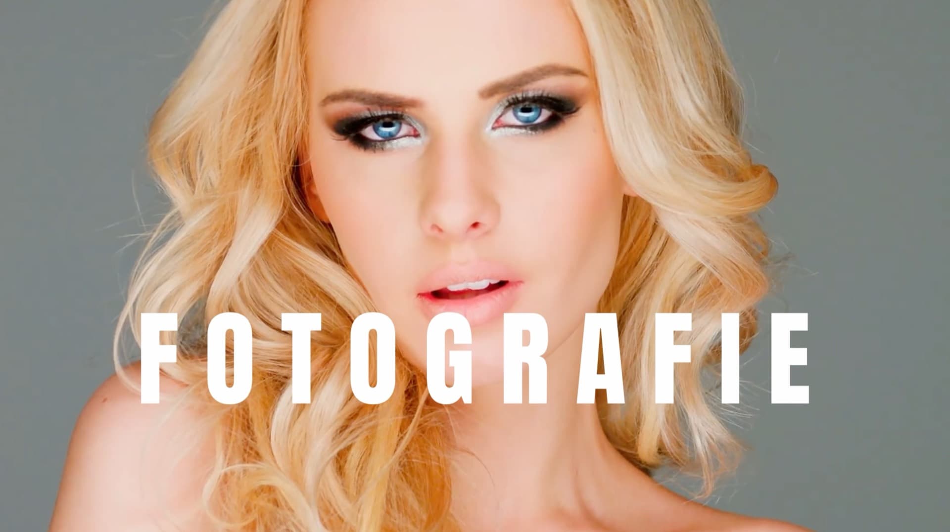 A close-up portrait of a person with long, wavy blonde hair and bright blue eyes, set against a plain gray background, with the word "FOTOGRAFIE" superimposed in bold white letters, showcasing a professional photography style.