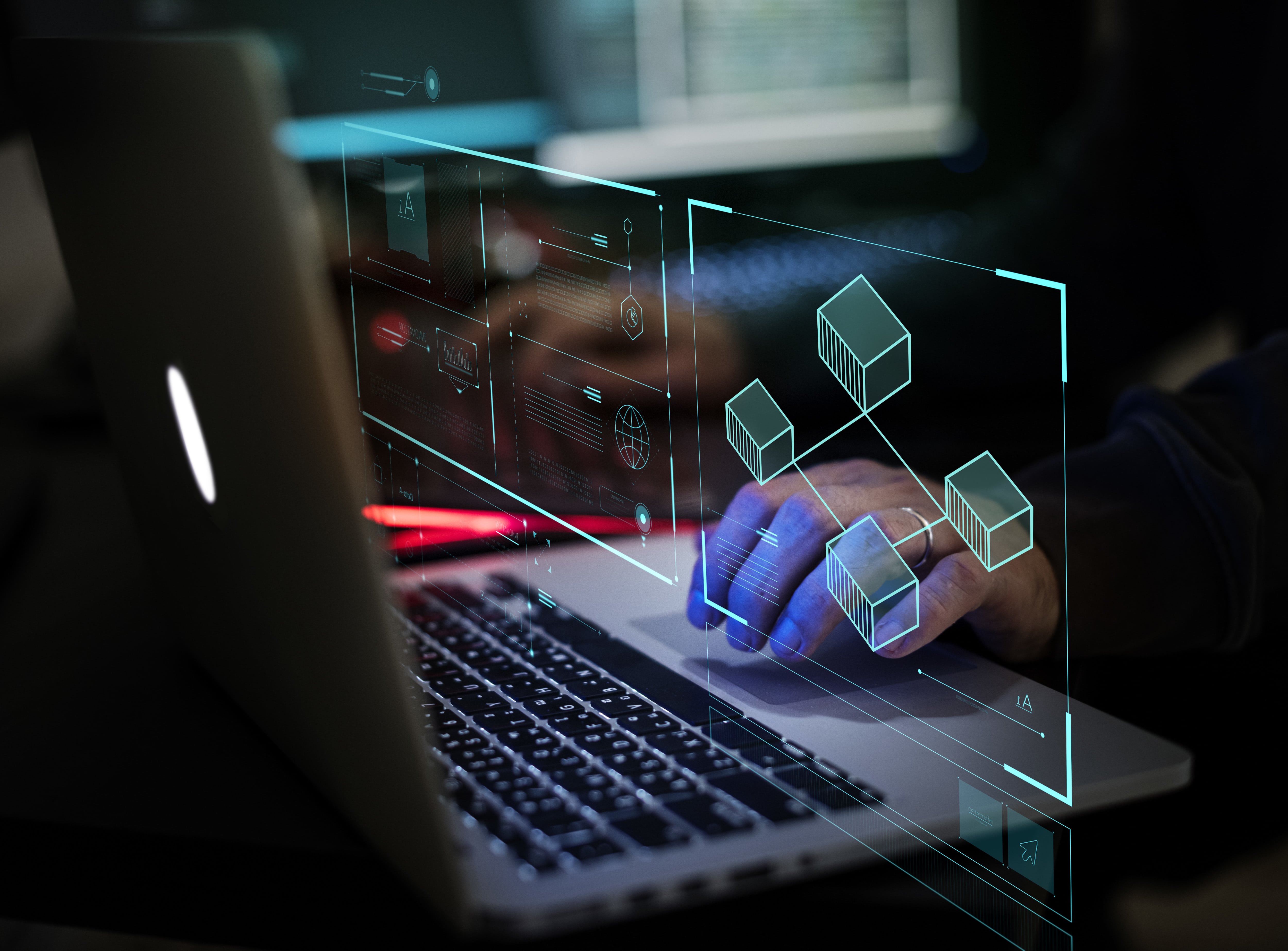 A person's hand on a laptop interacts with a futuristic, glowing blue holographic user interface displaying data visualizations and network blocks, illustrating concepts like blockchain, data analysis, and cybersecurity.