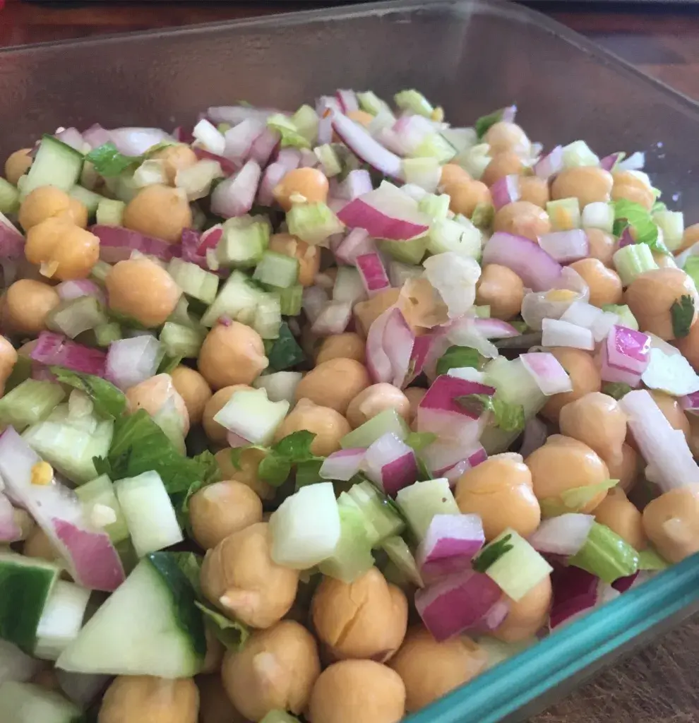 A vibrant chickpea salad in a glass dish, featuring diced red onions, crisp cucumber pieces, and fresh parsley.