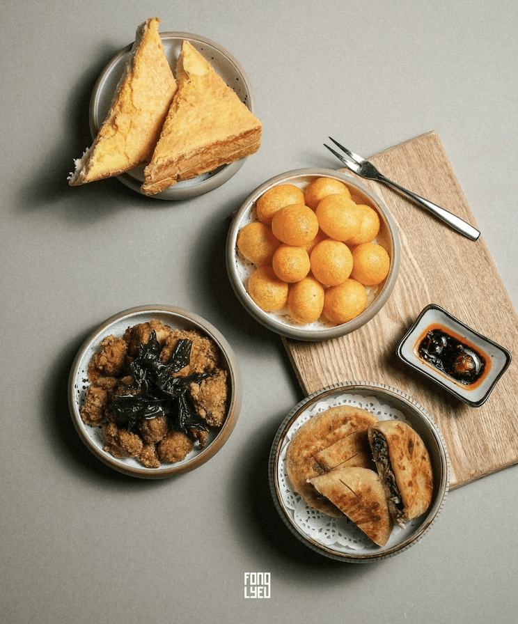 An assortment of Taiwanese dishes featuring golden fried chicken with greens, sweet potato balls, stuffed flatbreads, and toasted bread, served with a small dish of sauce.