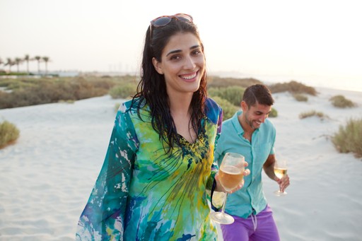 Woman holding ice cream and smiling while walking near a lake with a man in the background.