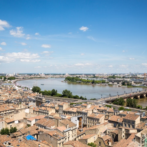 Aerial view of a city with densely packed buildings, a river, and a stone bridge under a clear blue sky.