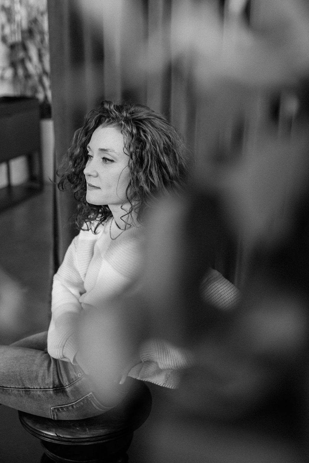 A thoughtful young person with dark hair gazes to the side, captured in soft black and white lighting.