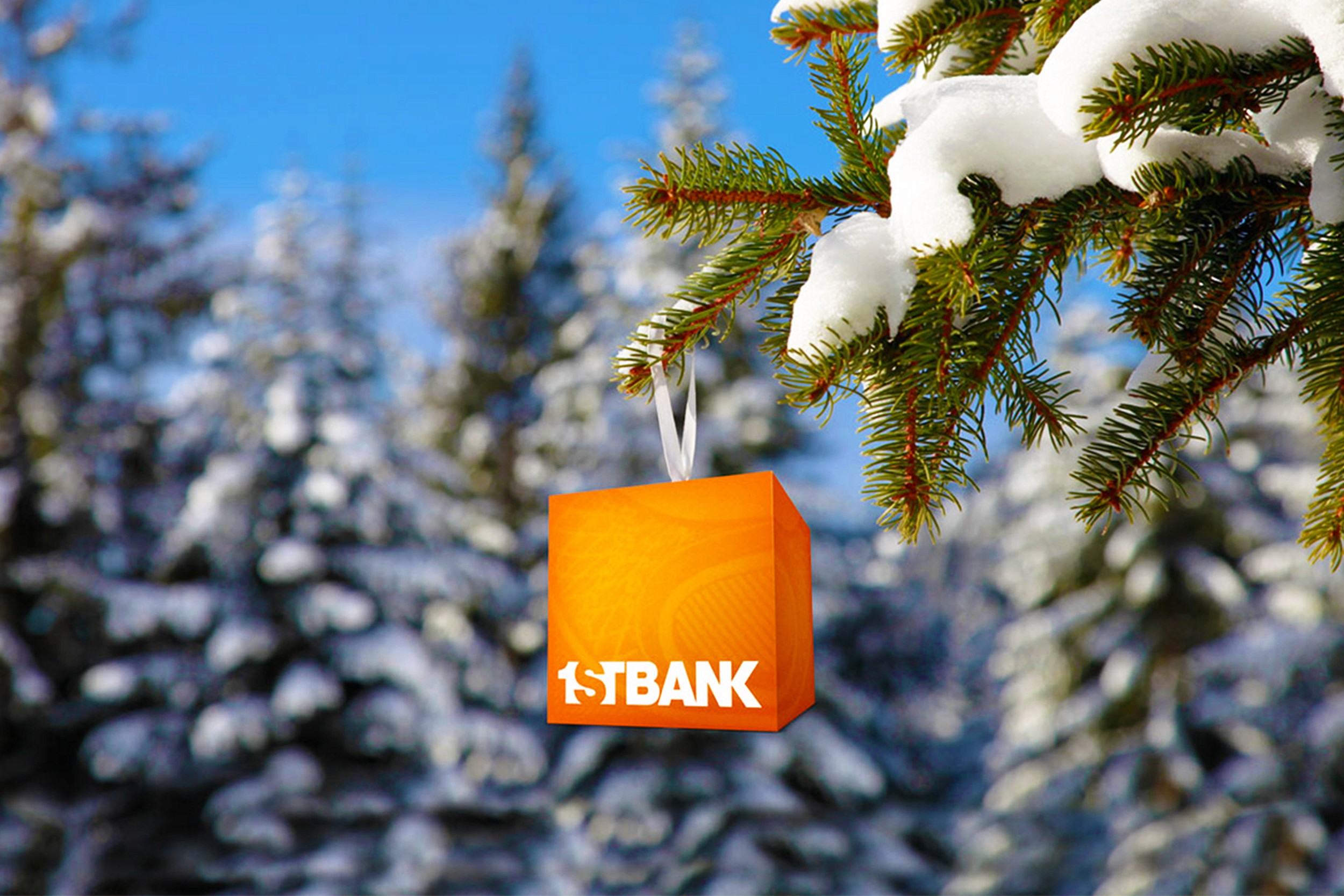 1stBank orange cube is hung on a snowy pine tree like an ornament. In the background is a snowy forest.