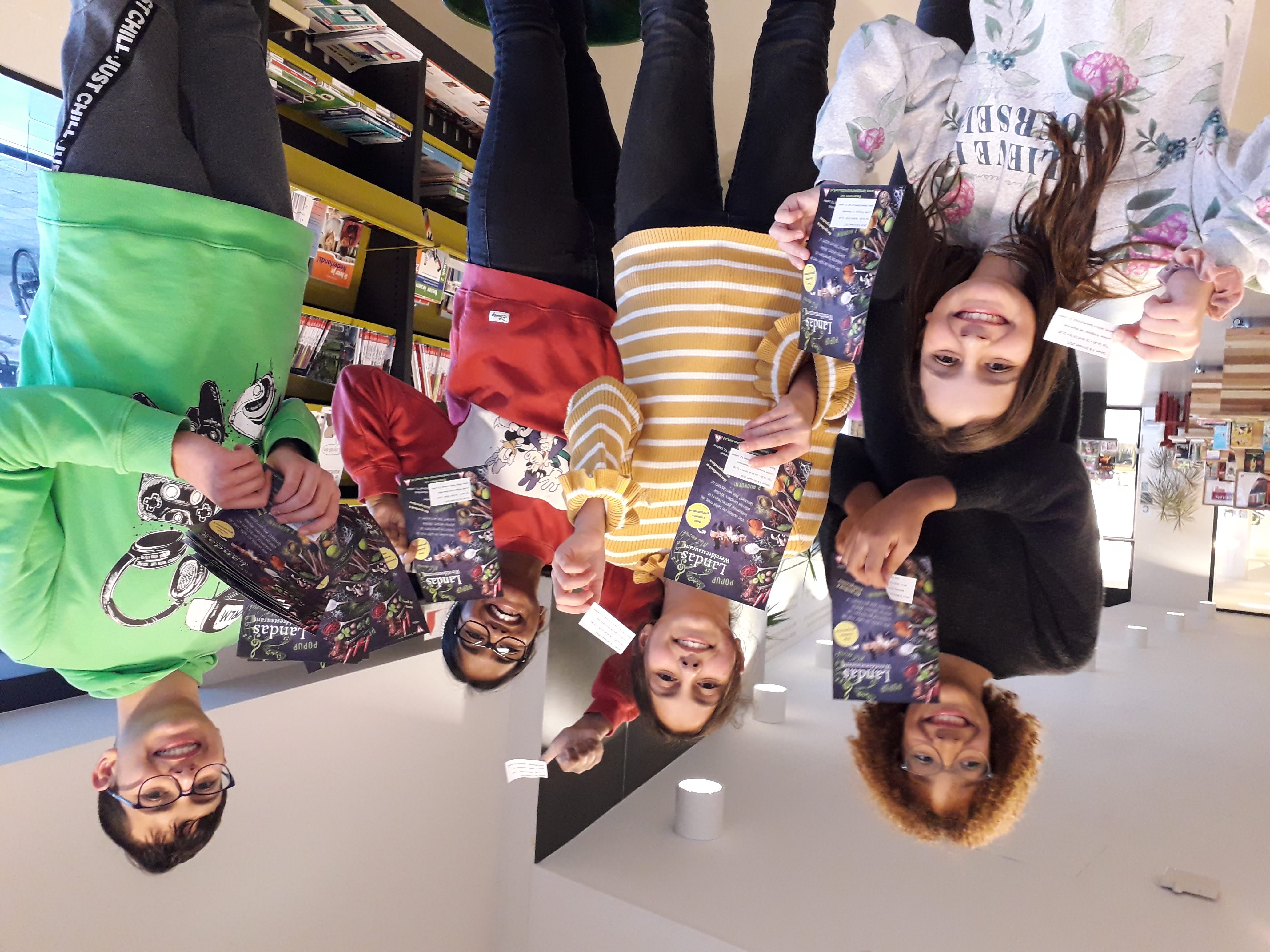 Twee jongens in groene truien met de tekst 'Wasted World' delen flyers uit op een markt