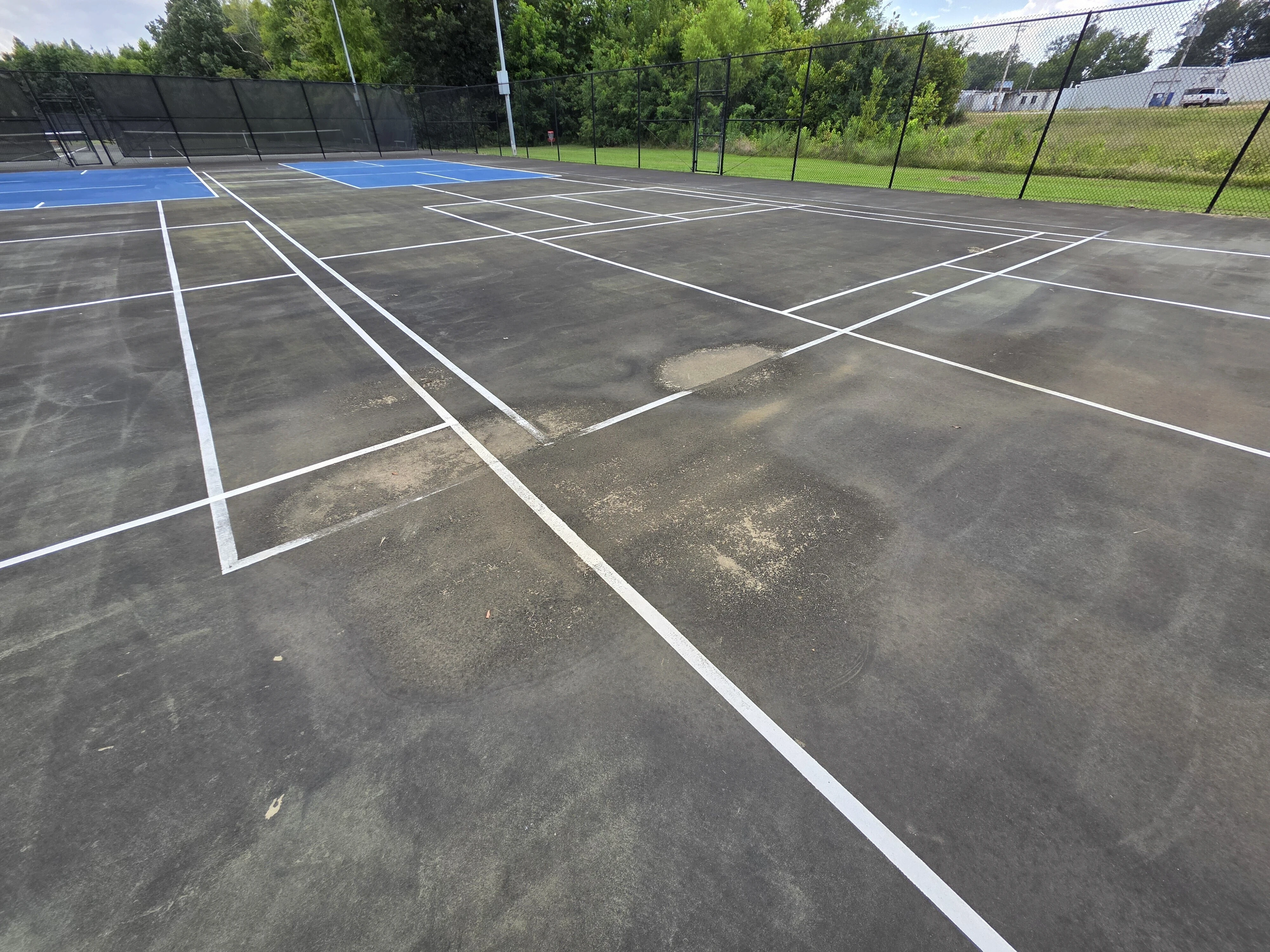 Aging pickleball courts with worn surfaces and patched areas before resurfacing in Corinth, MS