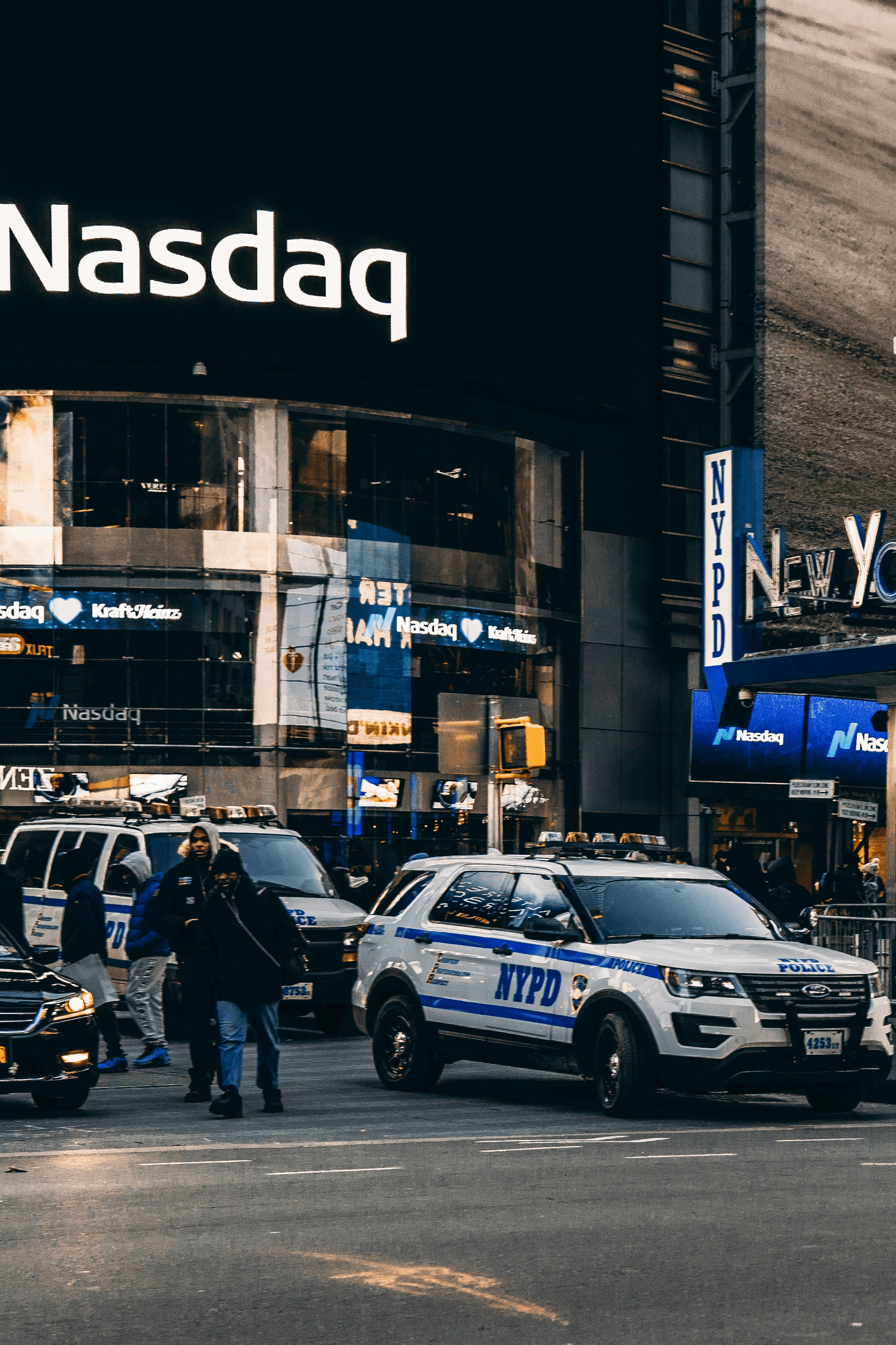 A man wearing glasses and a blazer working at a desk, writing in a notebook beside a computer monitor in a modern office.