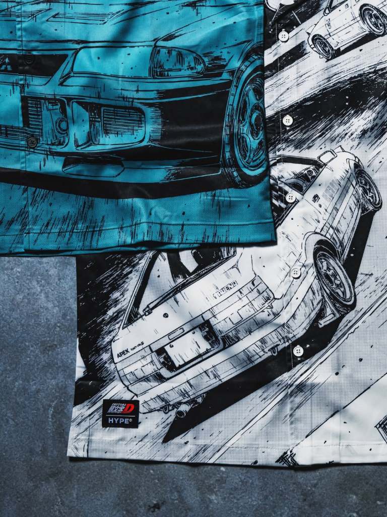 Close-up of a shirt featuring graphic designs inspired by Initial D, displaying stylized images of iconic cars against a colorful background.