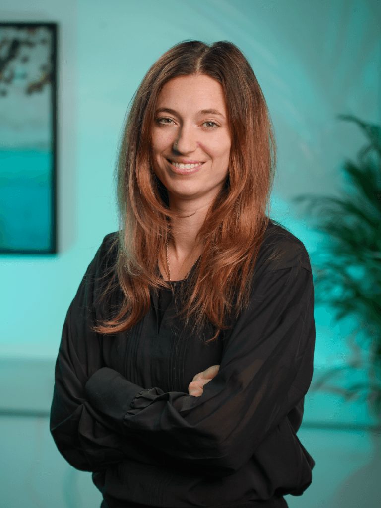 A woman with straight blonde hair wearing a light colored sweater looks away.