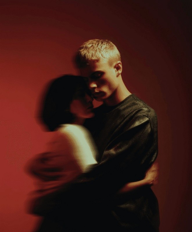Motion-blurred portrait of two figures against a warm red backdrop.