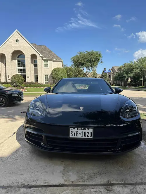 Front view of a shiny black Porsche Panamera parked in front of a luxury home after mobile detailing in Houston.