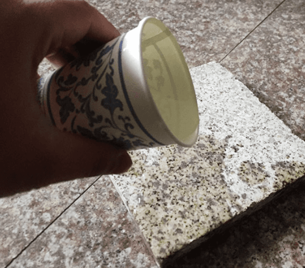 A person pouring water from a cup onto a granite tile to demonstrate the stone’s absorption properties.