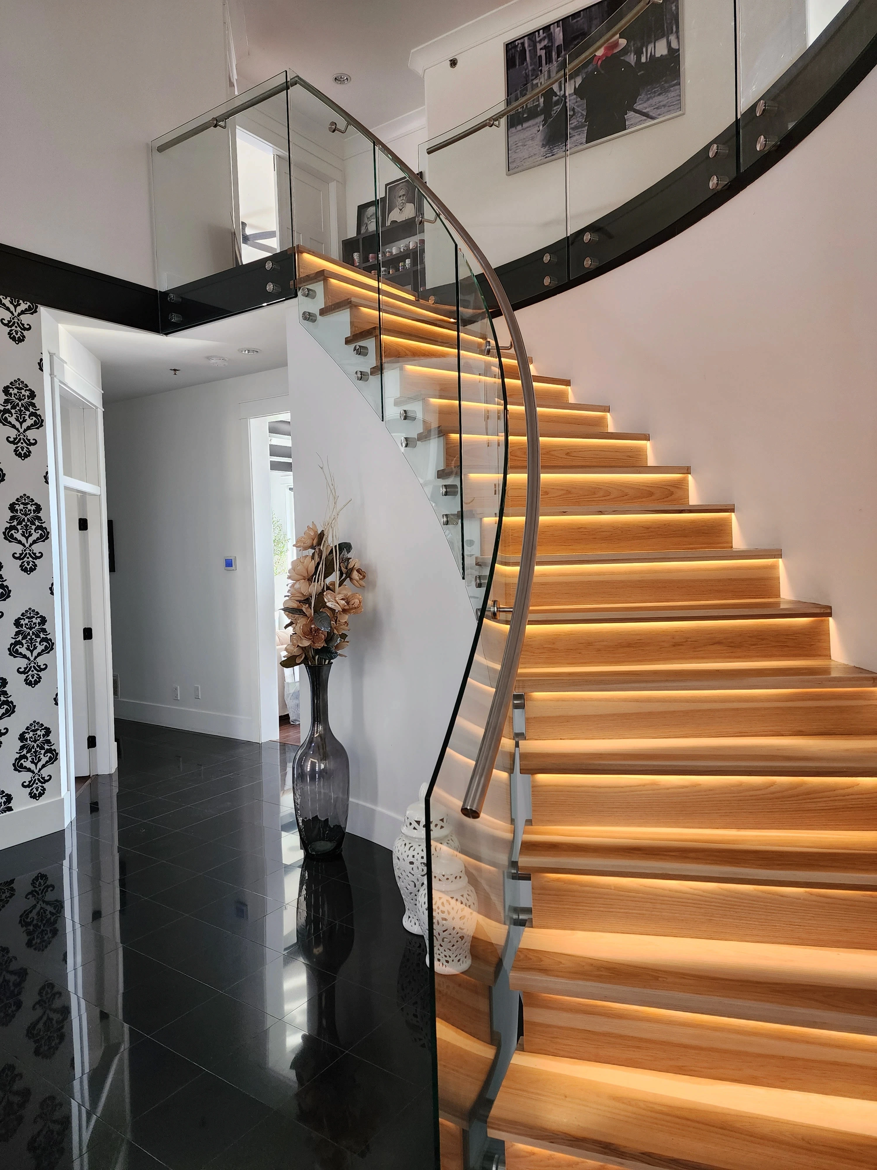 Curved frameless glass railing following a switchback staircase with a stainless handrail and LED-lit wood treads