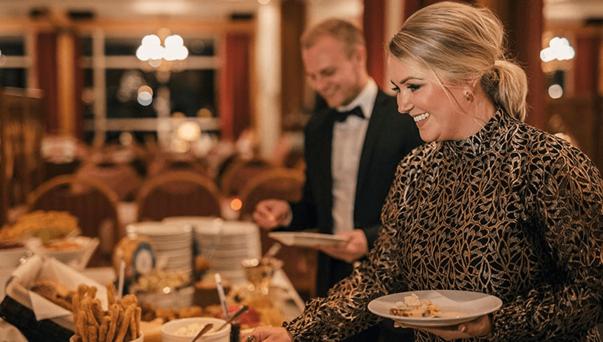 A man in formal attire and a woman in a patterned dress are serving food at a beautifully arranged dining table.