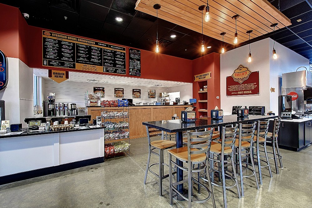 Modern restaurant interior with wooden accents, lively lighting, and seating area facing an open kitchen.