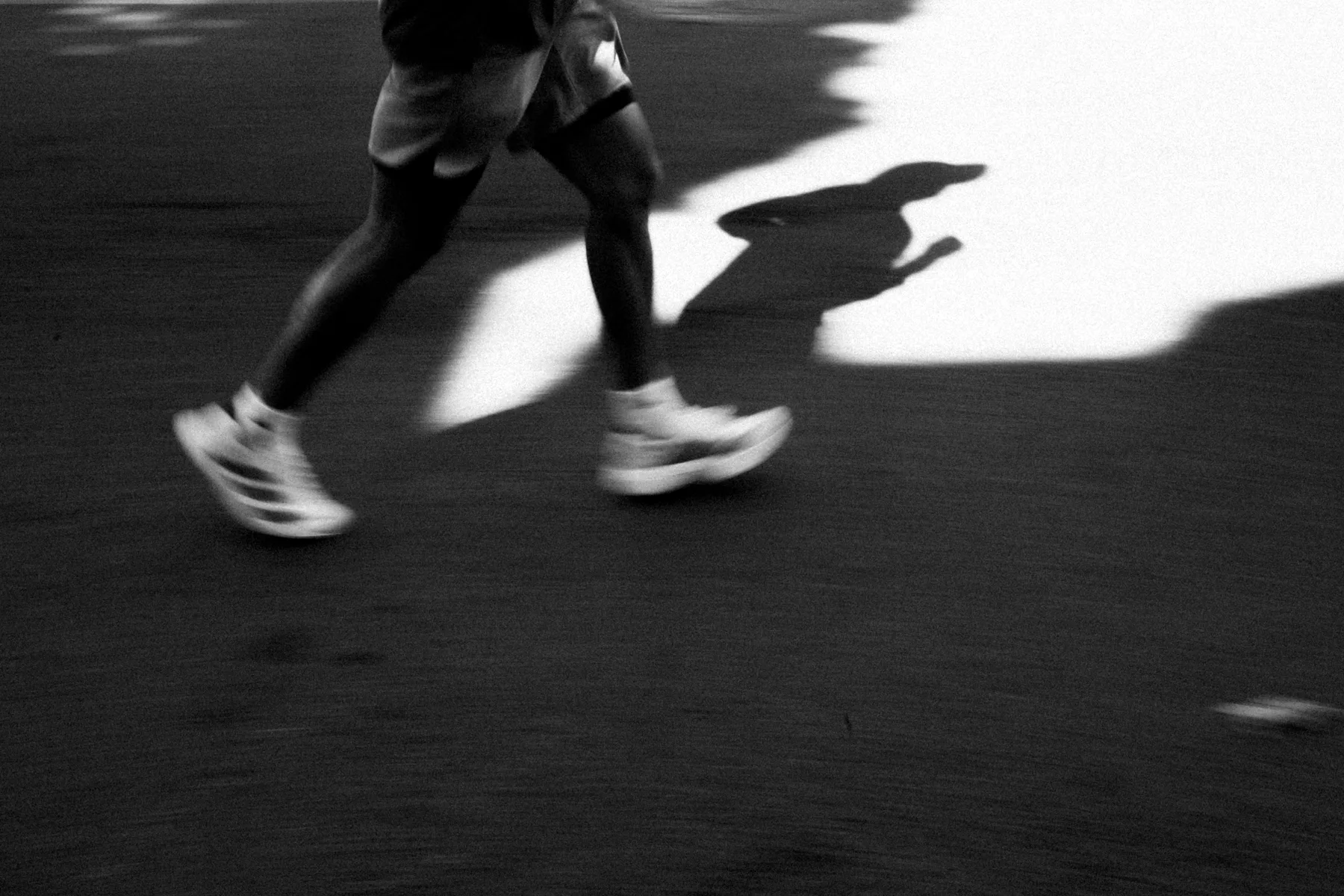 Black and white runner's legs crossing hard shadow