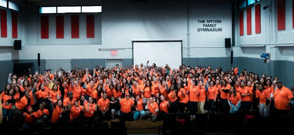 A large group of people in a gymnasium wearing orange staff shirts