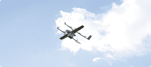 A drone with multiple propellers soars against a backdrop of a bright blue sky and scattered white clouds, showcasing advanced aerial technology and innovation.