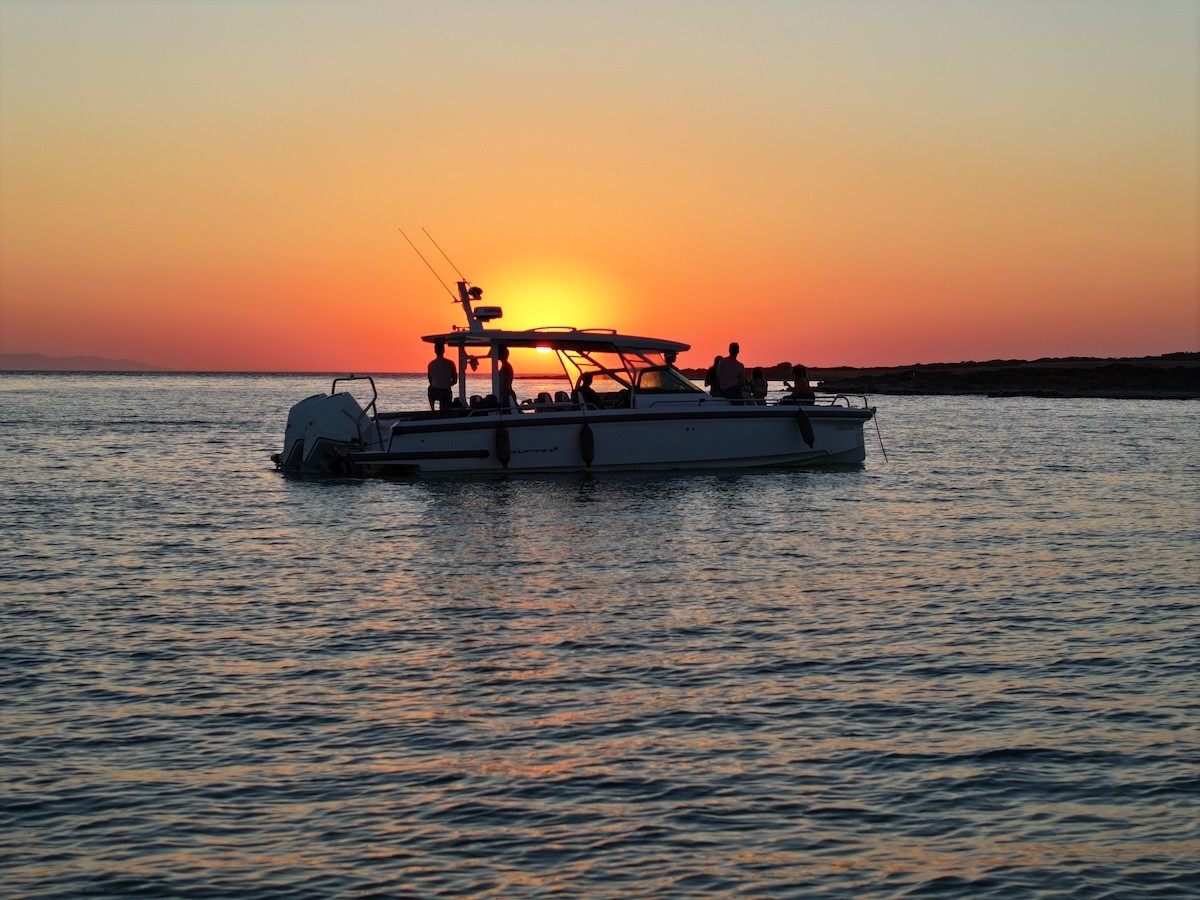White motor yacht with passengers aboard anchored in calm waters during golden sunset in the Cyclades.