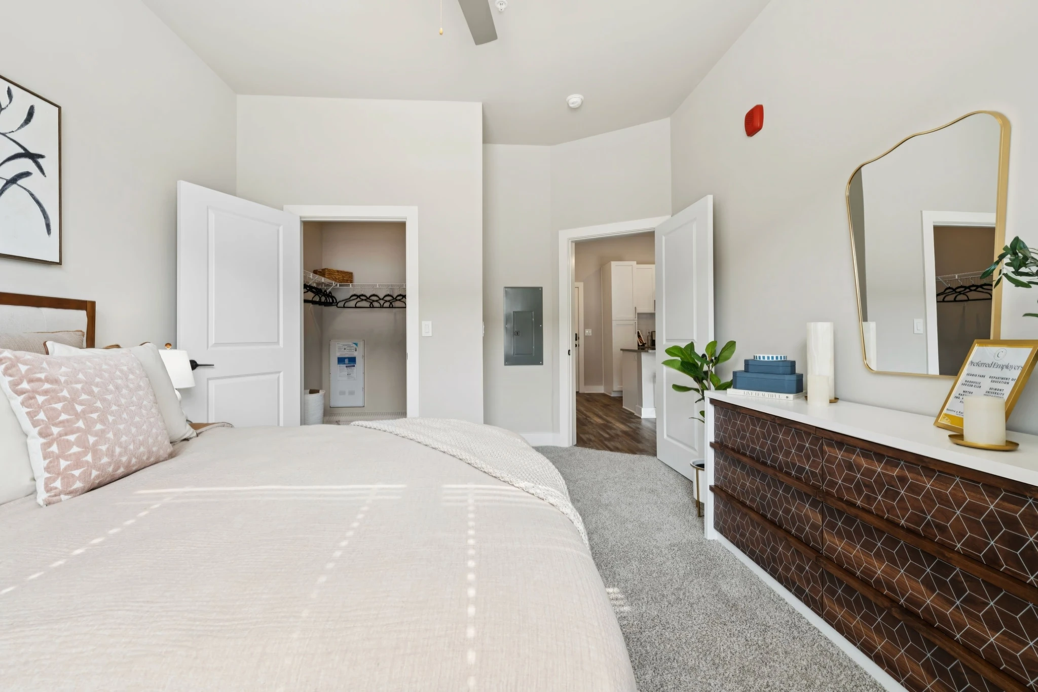 A well-furnished bedroom with a comfortable bed, a stylish dresser, and a mirror enhancing the space's brightness.
