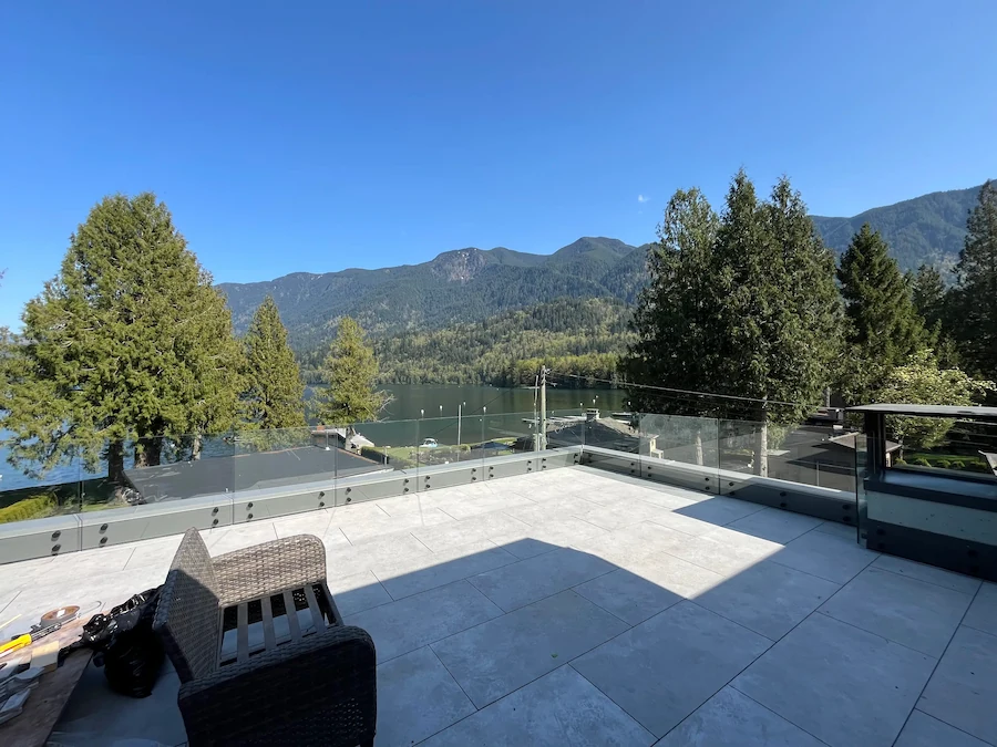Expansive lakefront view framed by frameless glass railing on an elevated patio, offering clear mountain and water vistas in British Columbia.