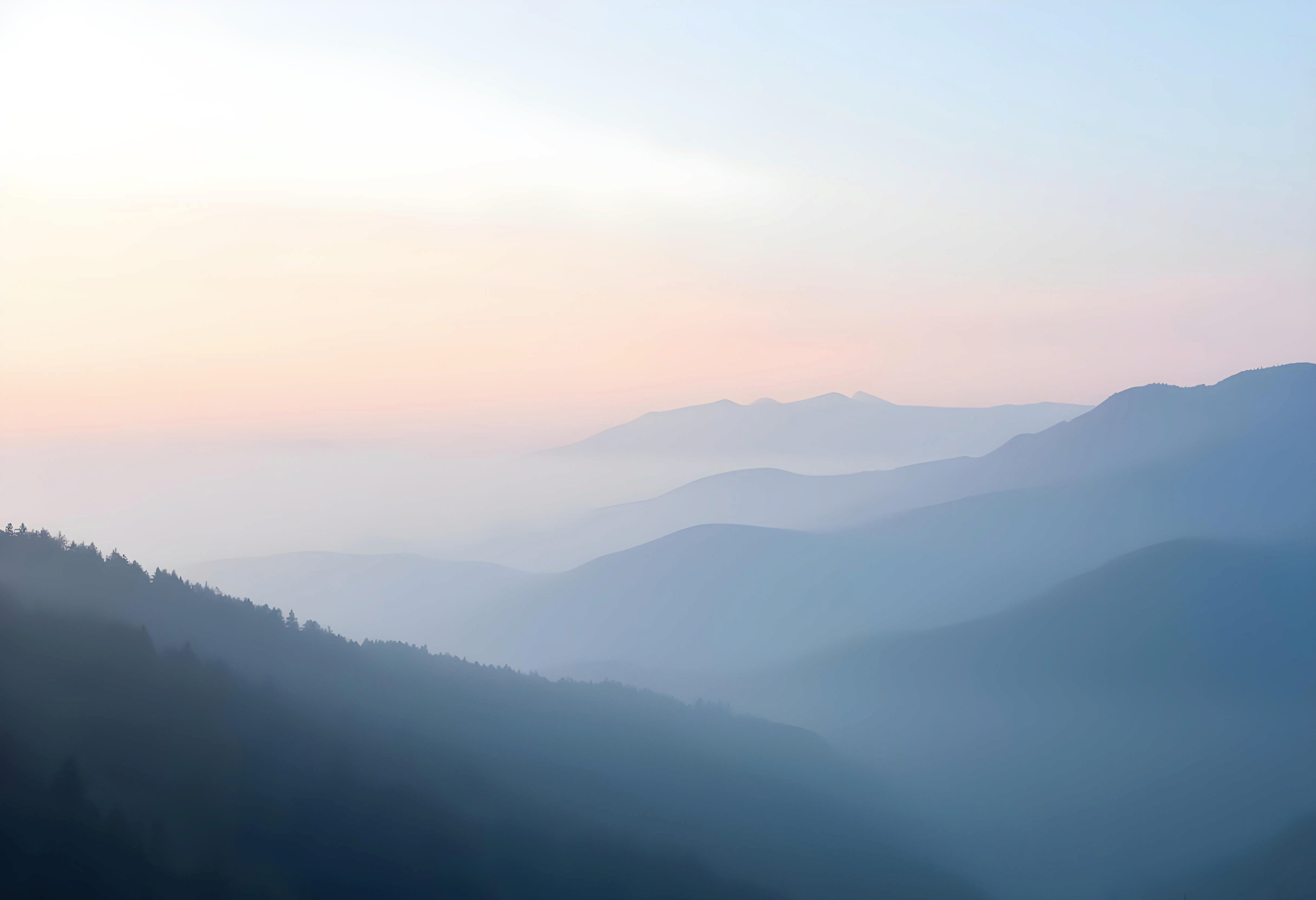 Soft, misty mountains stretch under a pale blue sky, creating a serene and tranquil landscape.