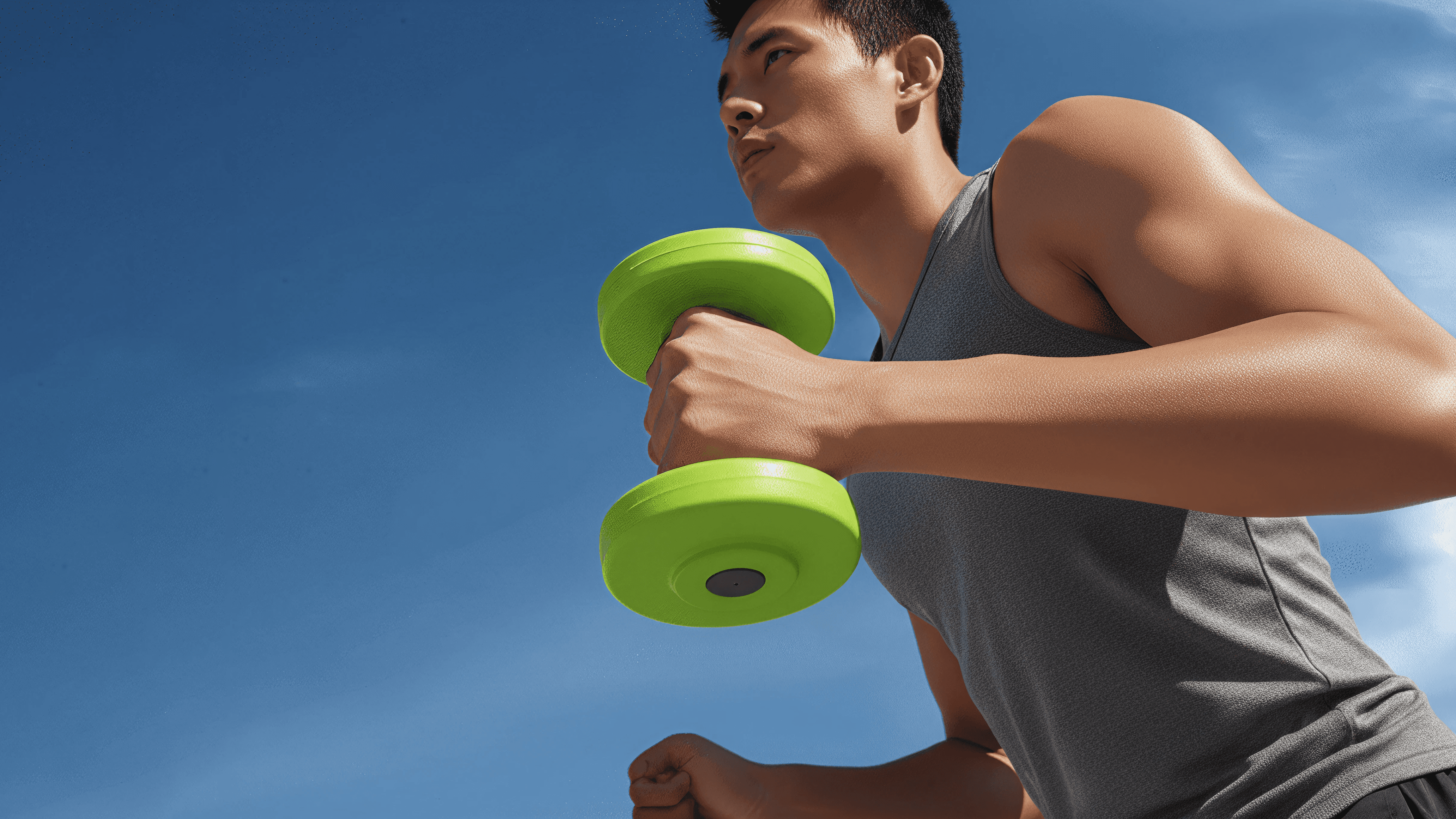 Man exercising outdoors with a green dumbbell, wearing a gray tank top, symbolizing strength and personal fitness training.
