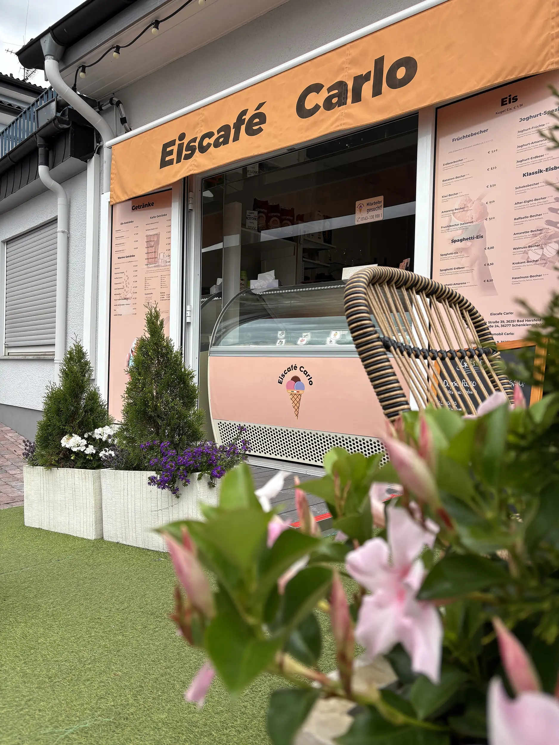 Eingangsbereich des Eiscafés mit Eisvitrine und Blumenbeeten