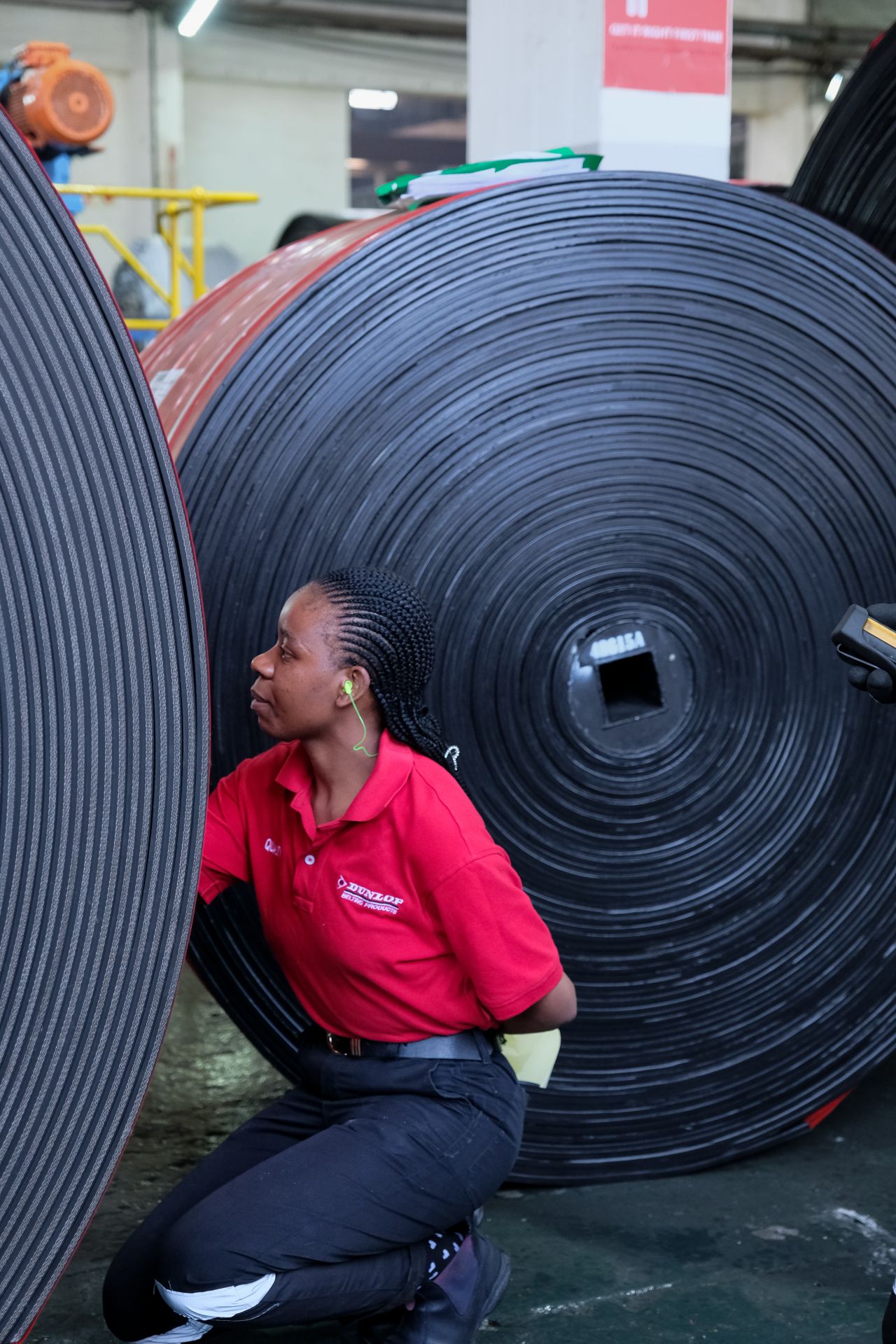 Smiling young woman with long hair standing against a dark green background, holding a finger to her chin.