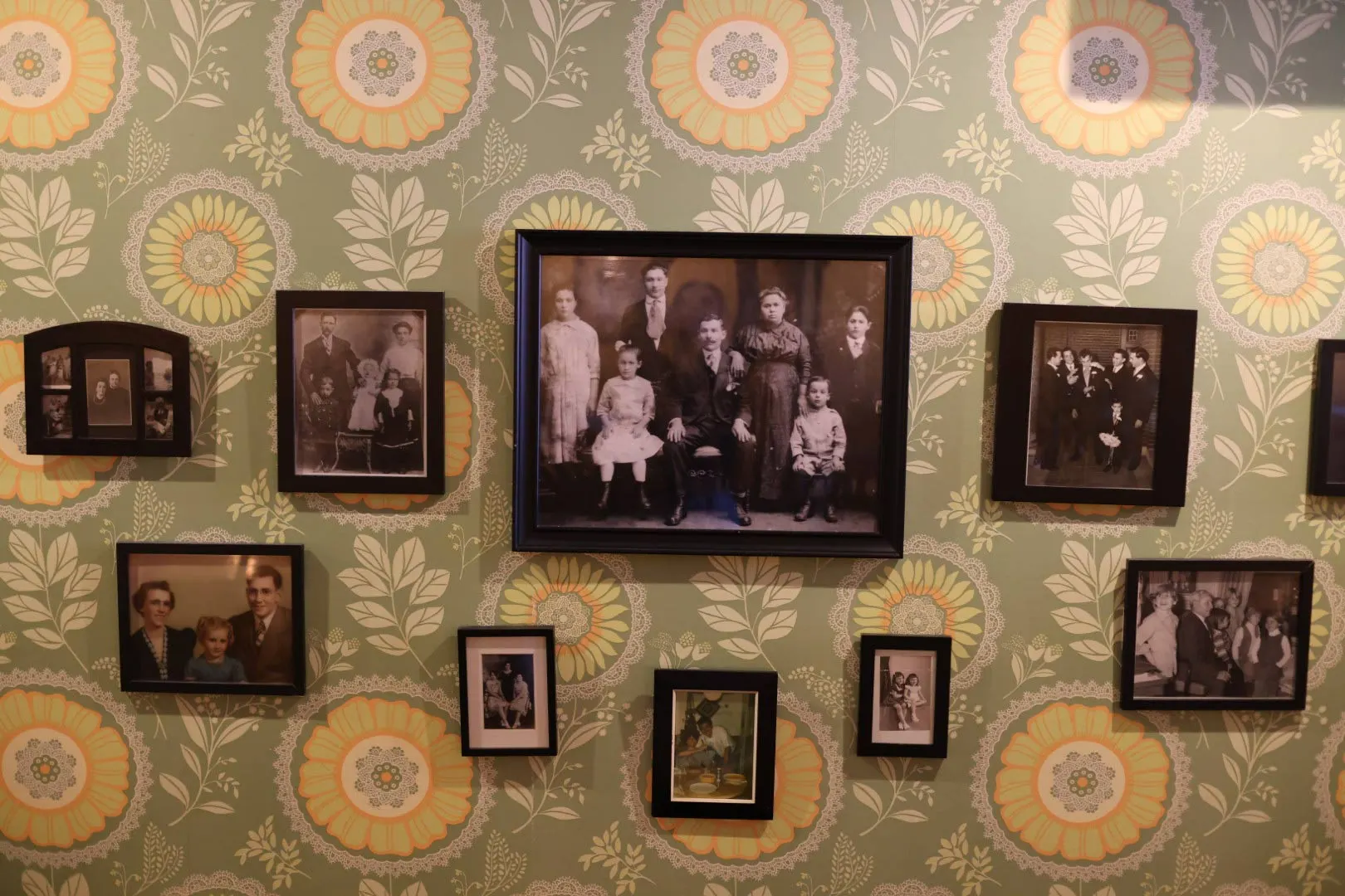 Wall of framed family photos on green patterned wallpaper