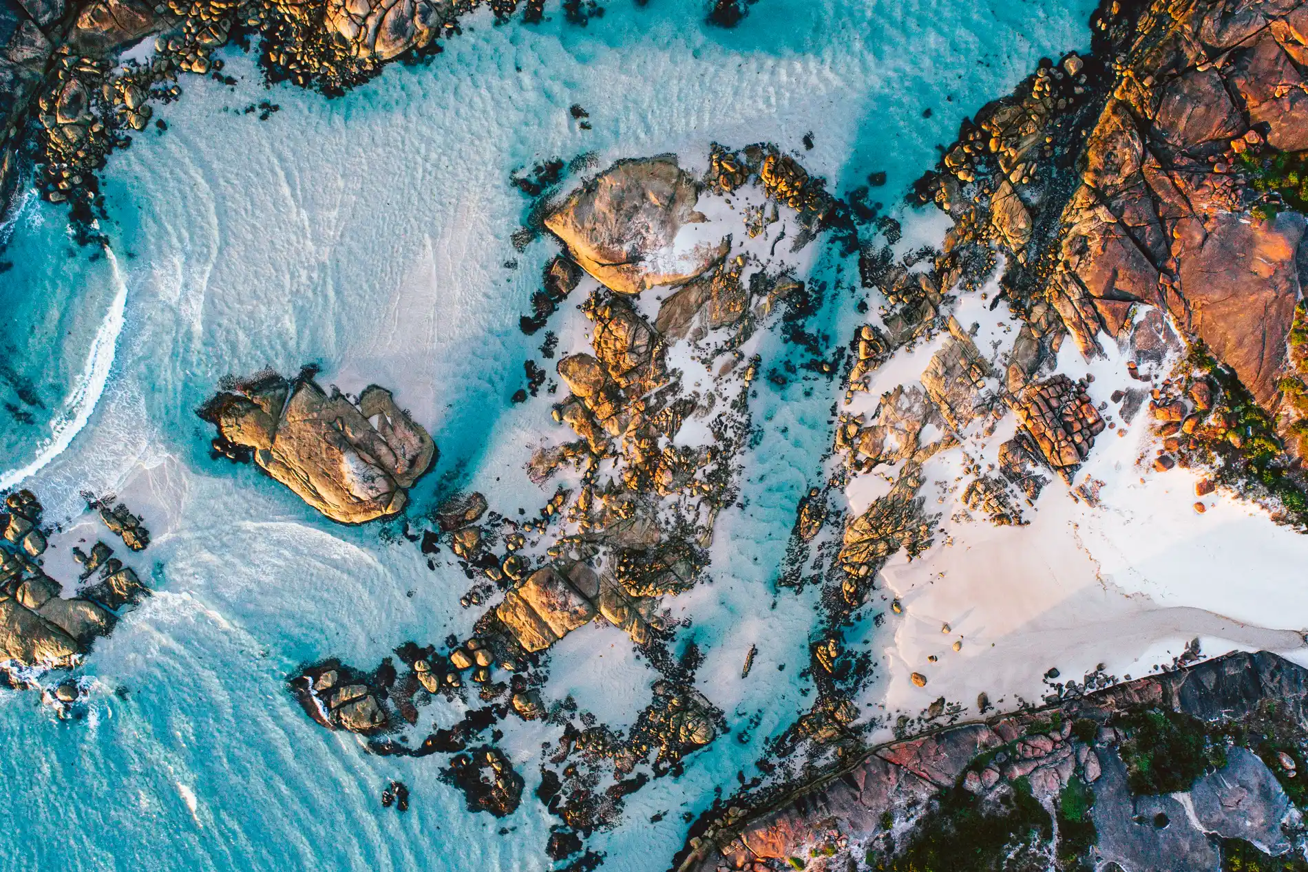 Aerial looking down on granite outcrops and reef in swirling turquoise water beside white sand