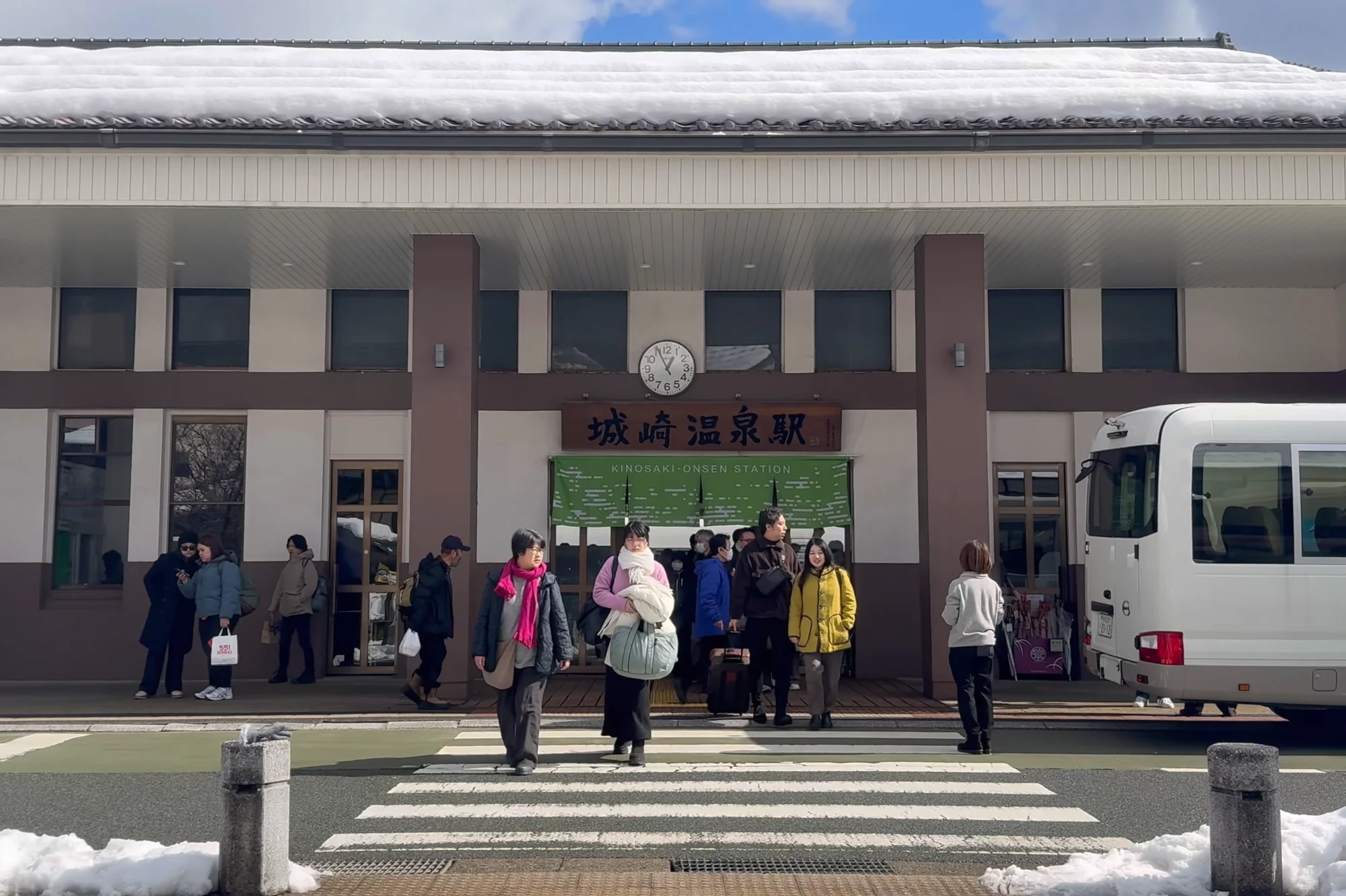 Travellers with luggage outside Kinosaki Onsen station in snow.