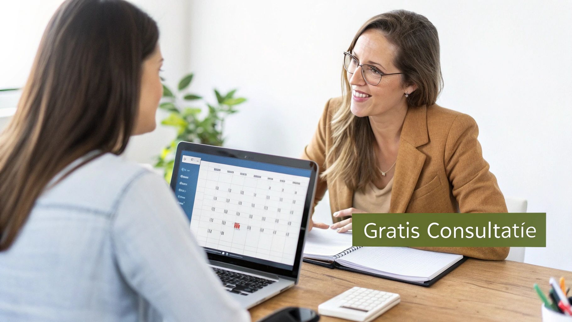 Twee vrouwen in gesprek, één kijkt naar een laptop met een kalender, de ander, een adviseur, glimlacht. Gratis consultatie.