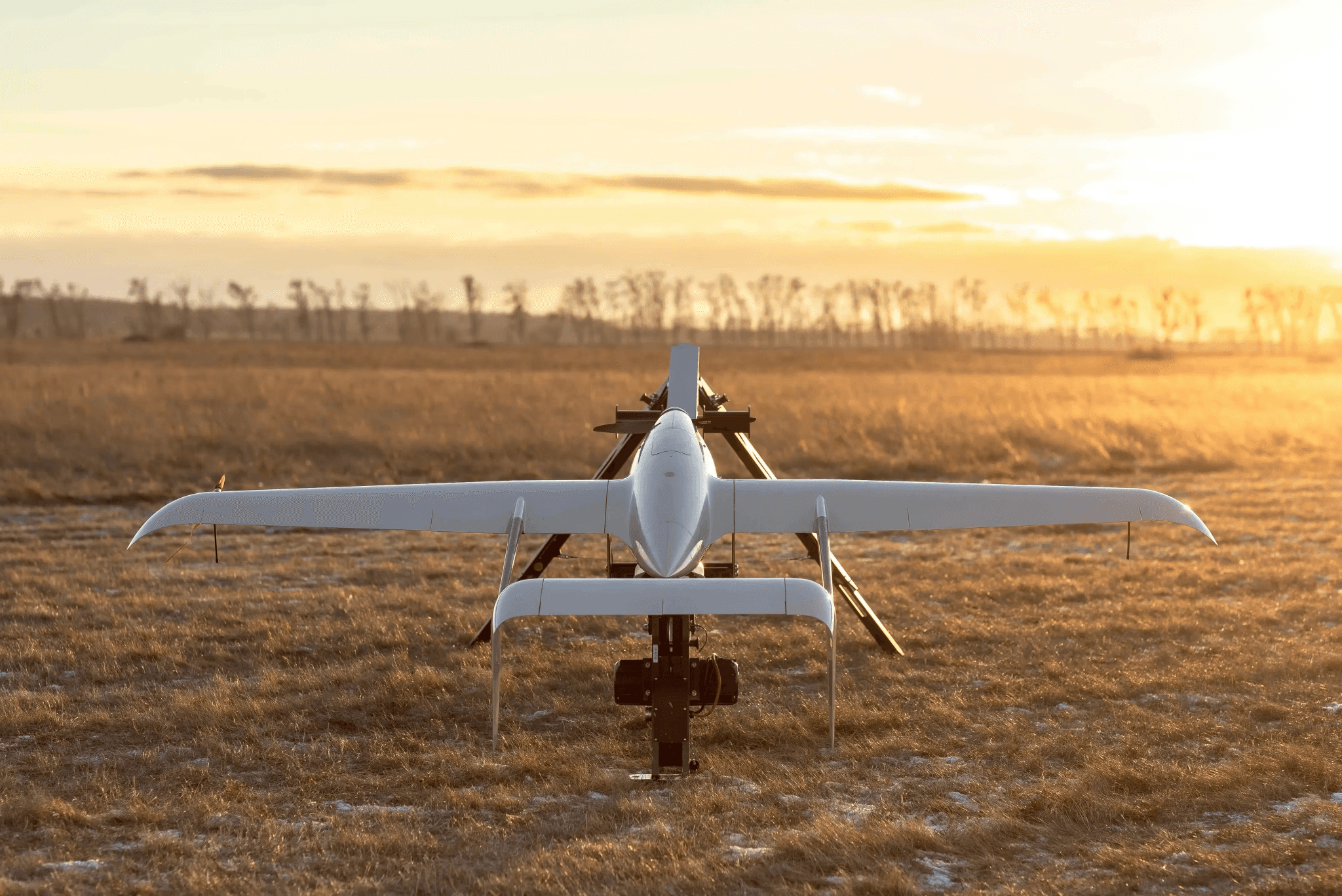 A sleek white drone is parked on a vast, sunlit field with dry grass under a clear, golden sky at sunset.VTOL drone before take off