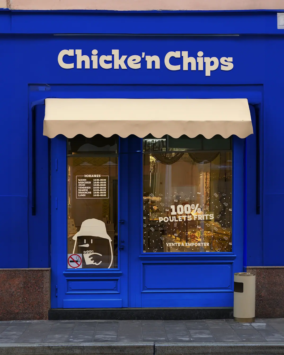 Devanture du restaurant Chicke'n Chips à Cholet, façade bleue Klein avec enseigne typographique blanche, marquise crème et vitrine avec mascotte illustrée.