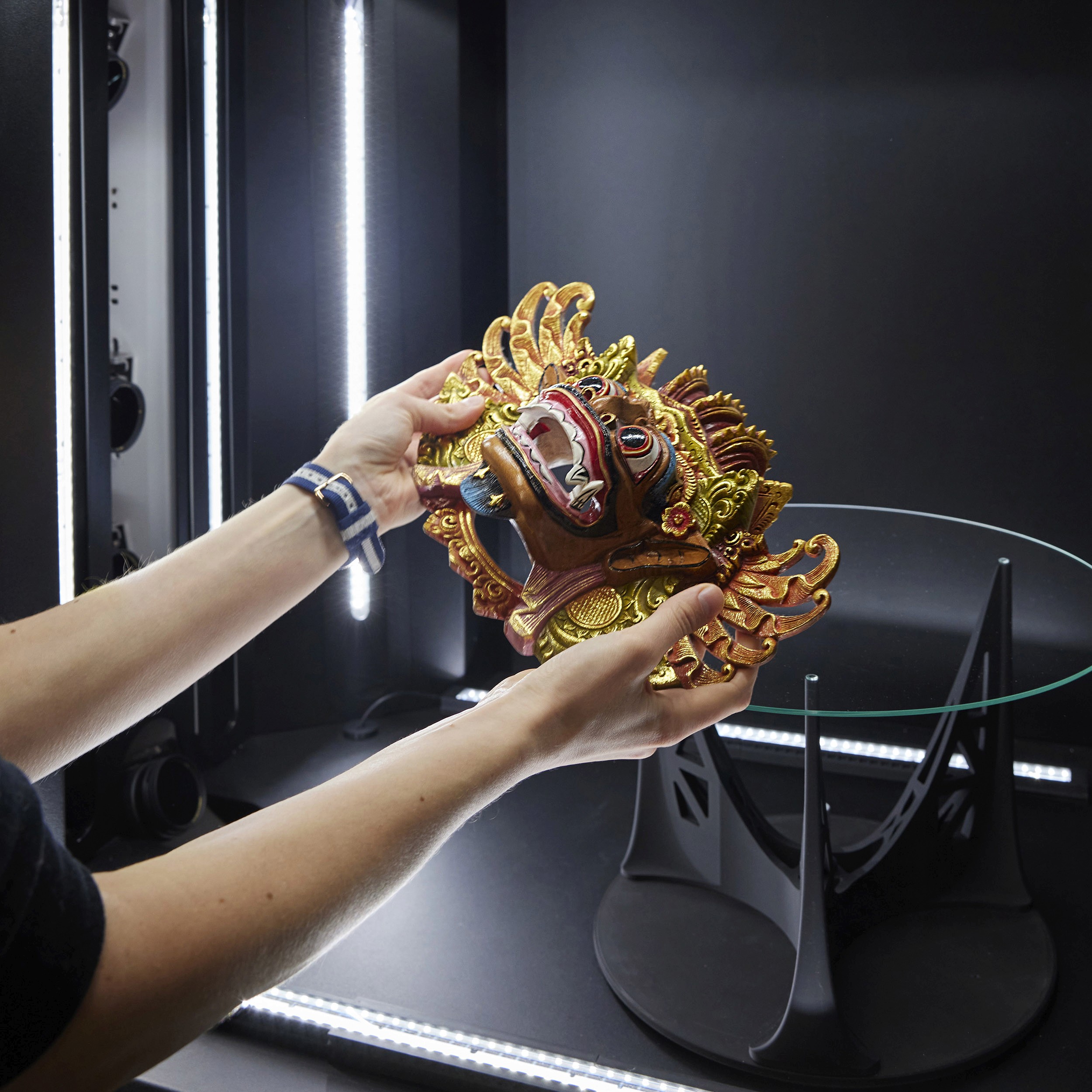 Hands holding the original Barong mask, placing it onto the glass turntable of the Momentum 2.0.