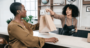 A cashier at a store hands a shopper a shopping bag.