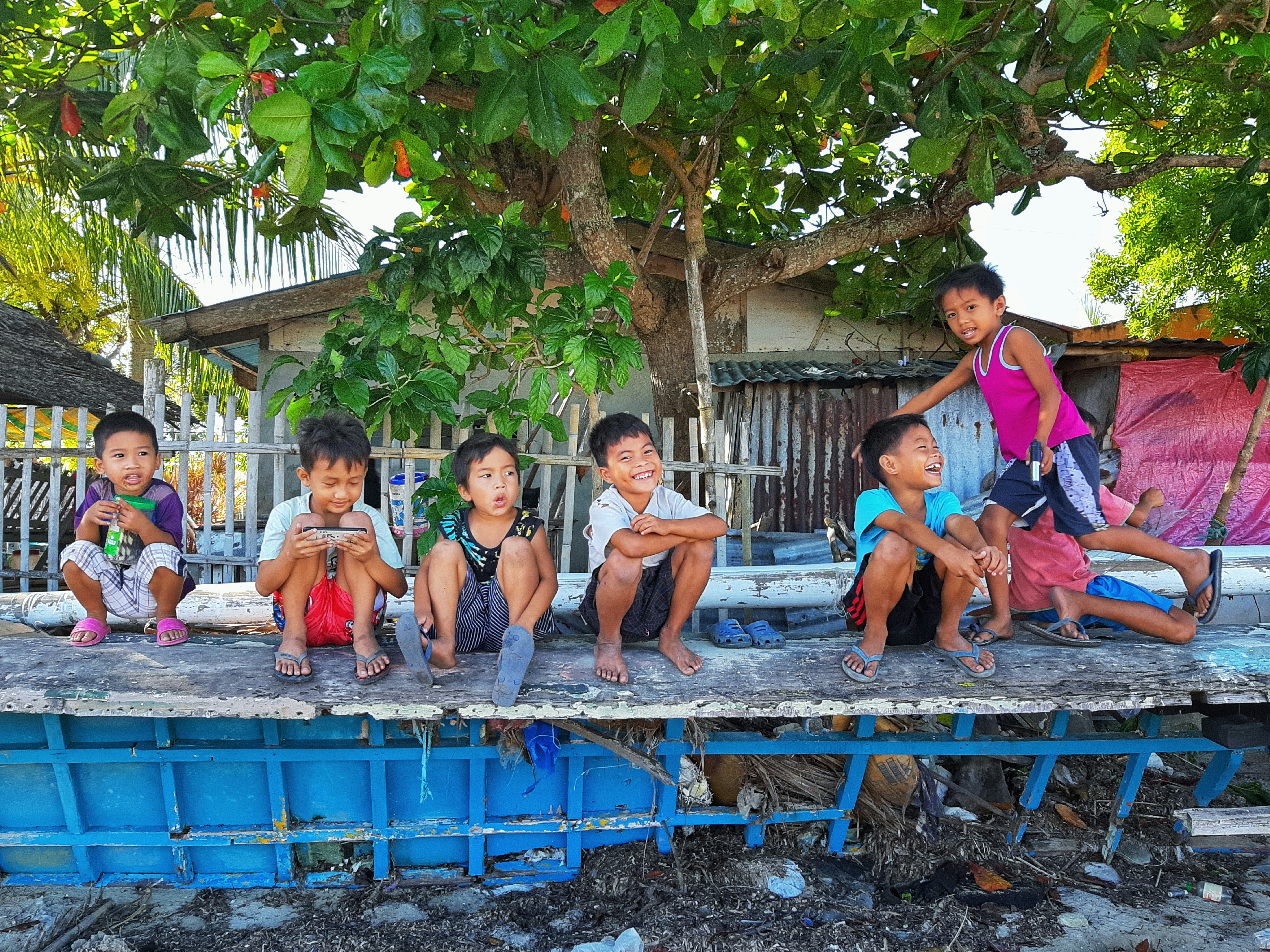Lachende Kinder sitzen auf einer alten Holzbank im Freien mit Baum im Hintergrund