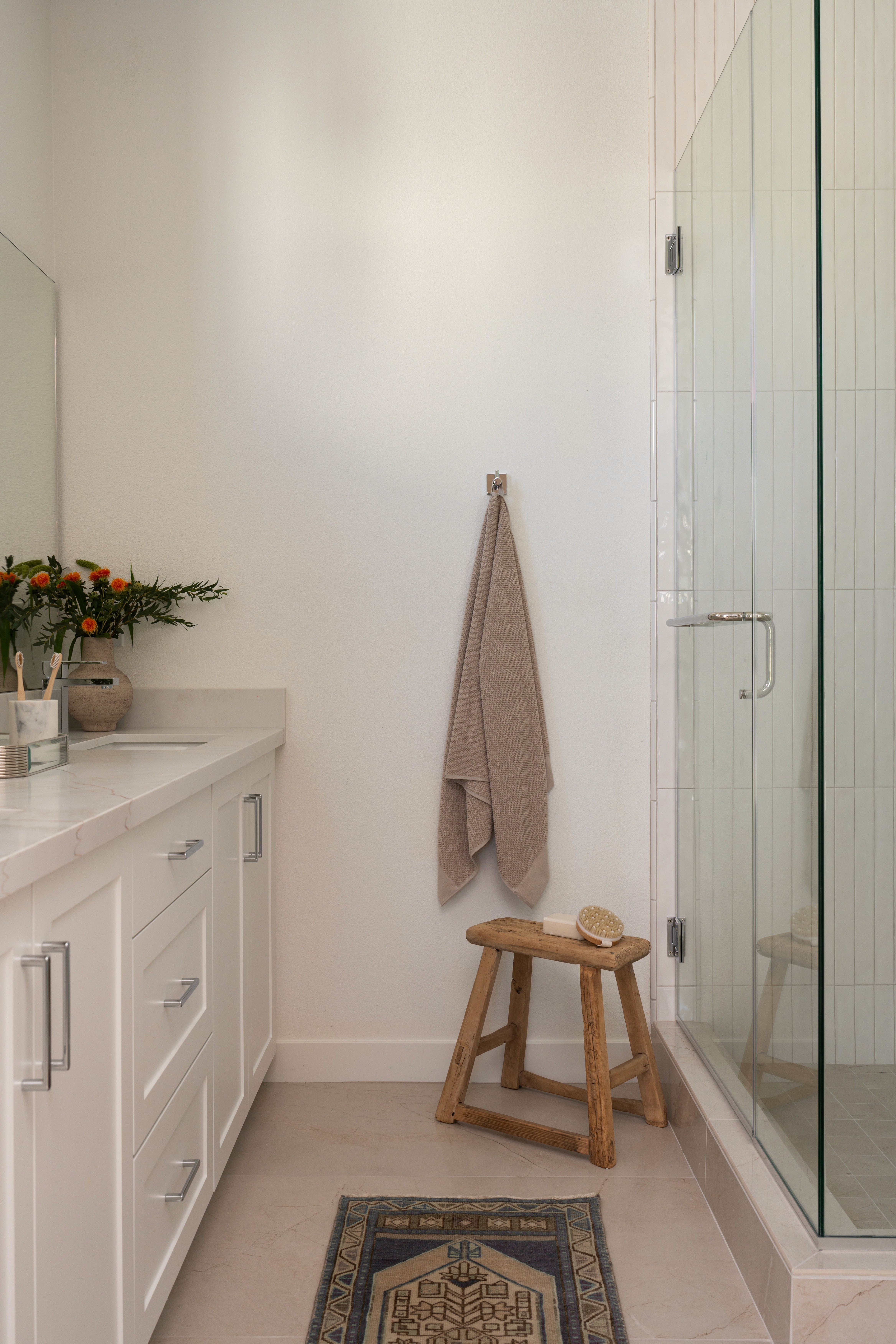 View of bathroom with decorative rug, stool, towel and greenery