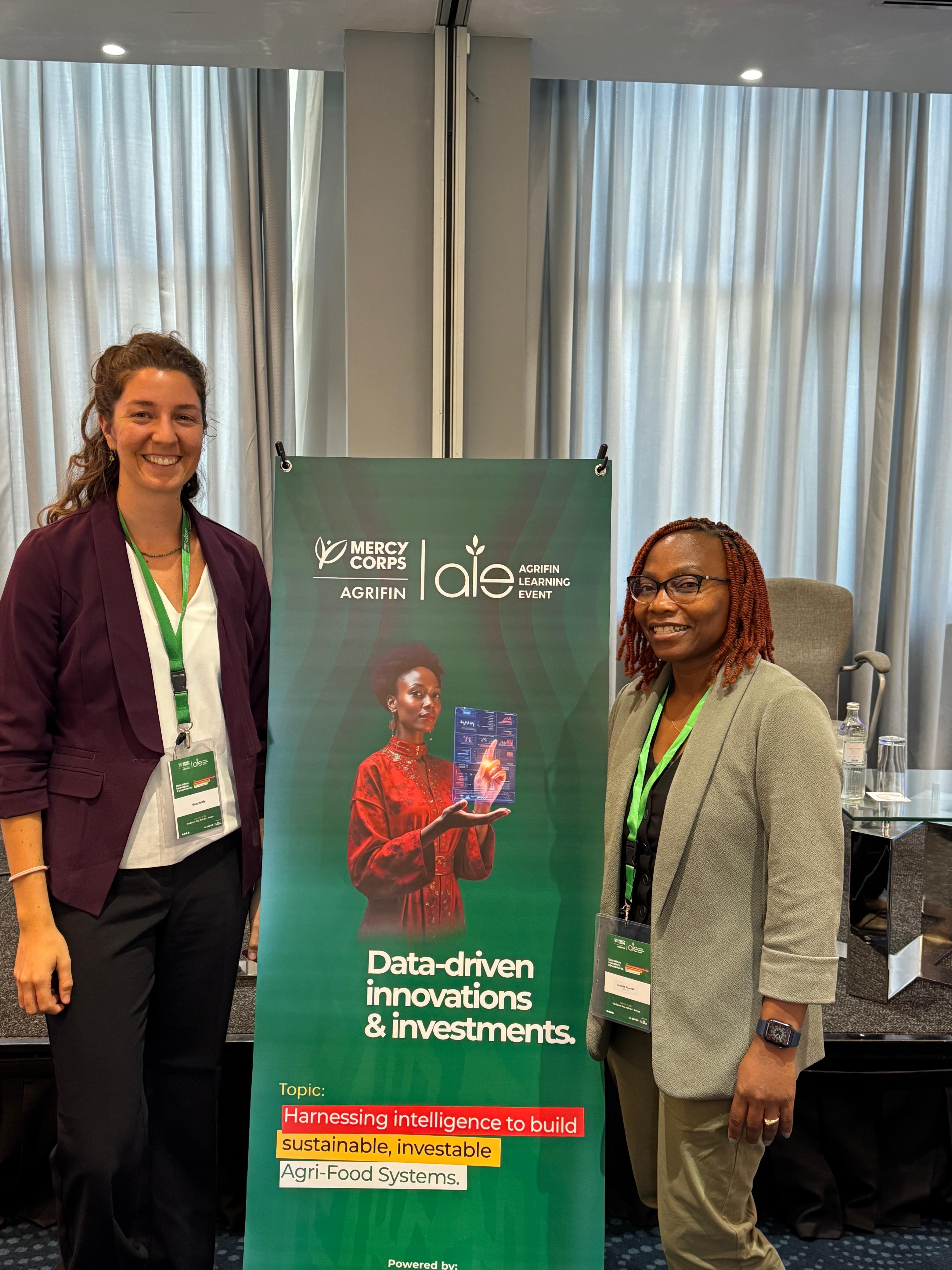 A smiling young man with crossed arms, wearing a plaid shirt and white t-shirt, poses against a dark background.
